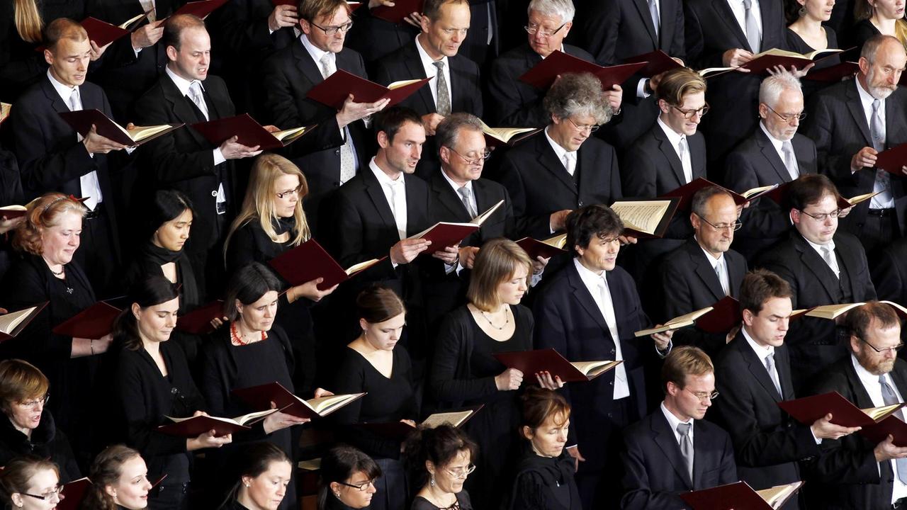 Männer und Frauen in schwarzer Kleidung und mit roten Gesangsbüchern stehen dicht an dicht in mehreren Reihen, die sich diagonal durch das Bild ziehen. Männer und Frauen in schwarzer Kleidung und mit roten Gesangsbüchern stehen dicht an dicht in mehreren Reihen, die sich diagonal durch das Bild ziehen.