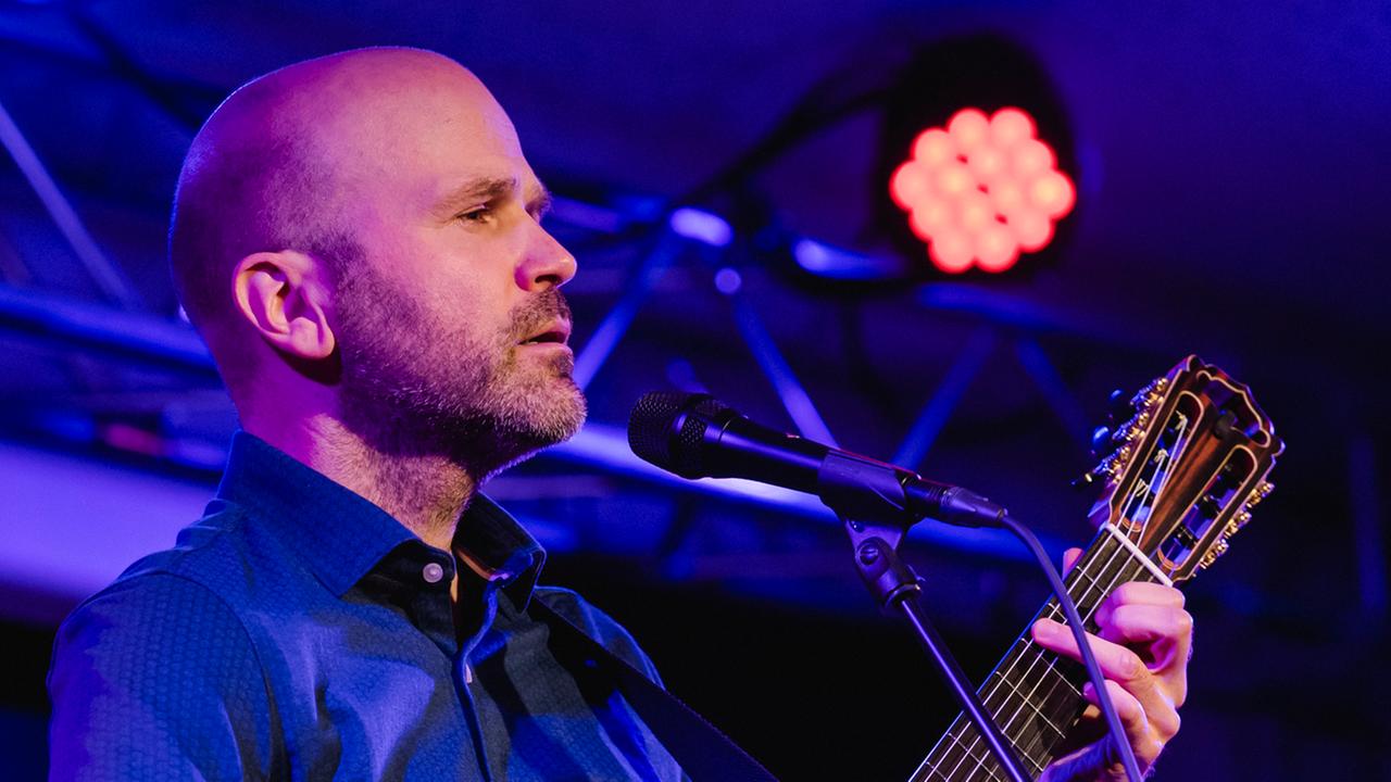 Ein Mann mit Gitarre steht auf einer Bühne Ein Mann mit Gitarre steht auf einer Bühne