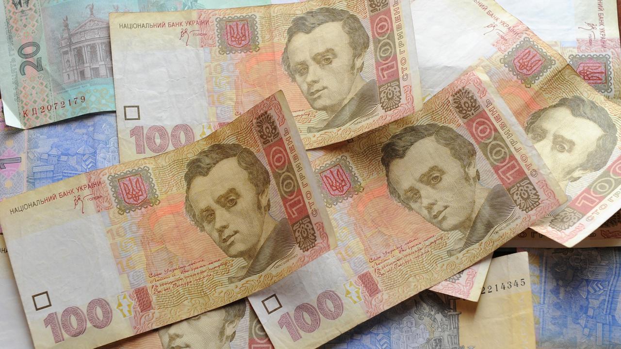 Auf einem Tisch liegen ein Dutzend Geldscheine der ukrainischen Währung Hrywnja, vor allem 1-, 20- und 100-Hrywnja-Scheine.