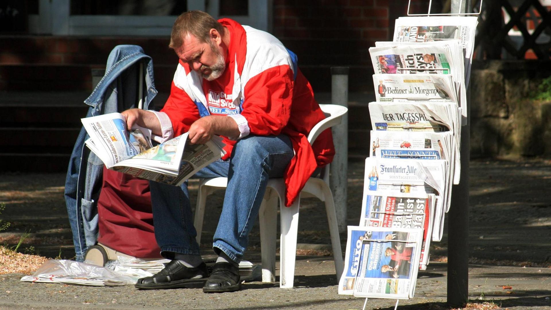 Ein Zeitungsverkäufer liest neben seinem Stand in einer Zeitung Ein Zeitungsverkäufer liest neben seinem Stand in einer Zeitung