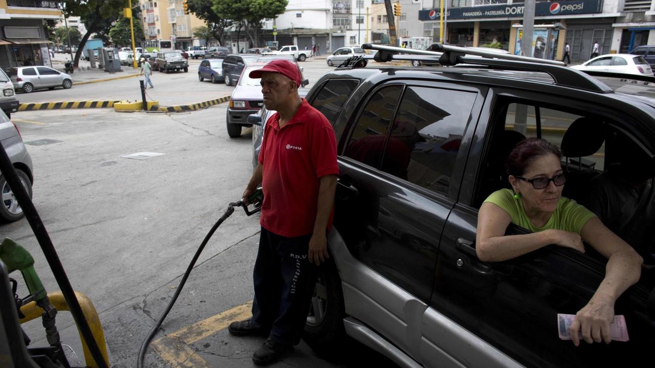 Eine Frau im Auto an einer Tankstelle. Ein Angestellter füllt ihren Tank.