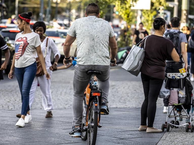 Ein Fahrradfahrer fährt auf einem Gehweg zwischen Passanten in Berlin-Kreuzberg.