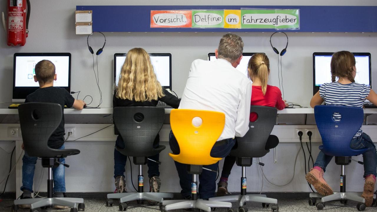 Schüler und ihr Lehrer arbeiten in einem Klassenraum einer Grundschule an Computern. Schüler und ihr Lehrer arbeiten in einem Klassenraum einer Grundschule an Computern.