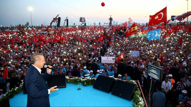 Sie sehen den türkischen Präsidenten Erdogan, dahinter eine große Menschenmenge.