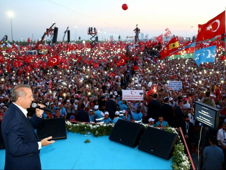 Sie sehen den türkischen Präsidenten Erdogan, dahinter eine große Menschenmenge.