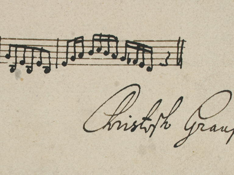 Unterhalb einer handgeschriebenen Notenzeile steht die Unterschrift des Komponisten.
