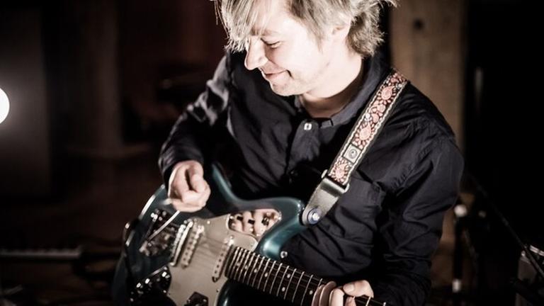 Ein Mann spielt Gitarre auf einer Bühne. Im Hintergrund brennt ein Scheinwerfer. Ein Mann spielt Gitarre auf einer Bühne. Im Hintergrund brennt ein Scheinwerfer.