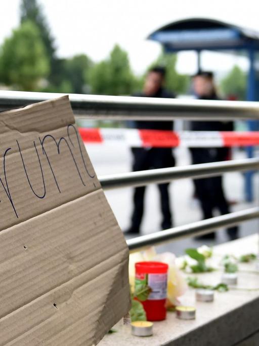 Ein Pappschild mit der Aufschrift "Warum?" und Blumen liegen am Eingang der U-Bahn "Olympia Einkaufszentrum" in München.