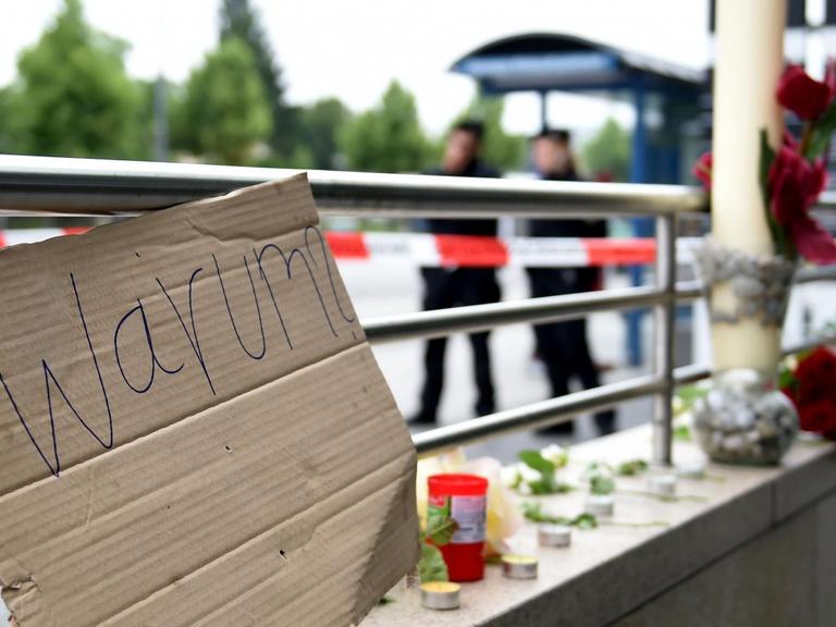 Ein Pappschild mit der Aufschrift "Warum?" und Blumen liegen am Eingang der U-Bahn "Olympia Einkaufszentrum" in München.