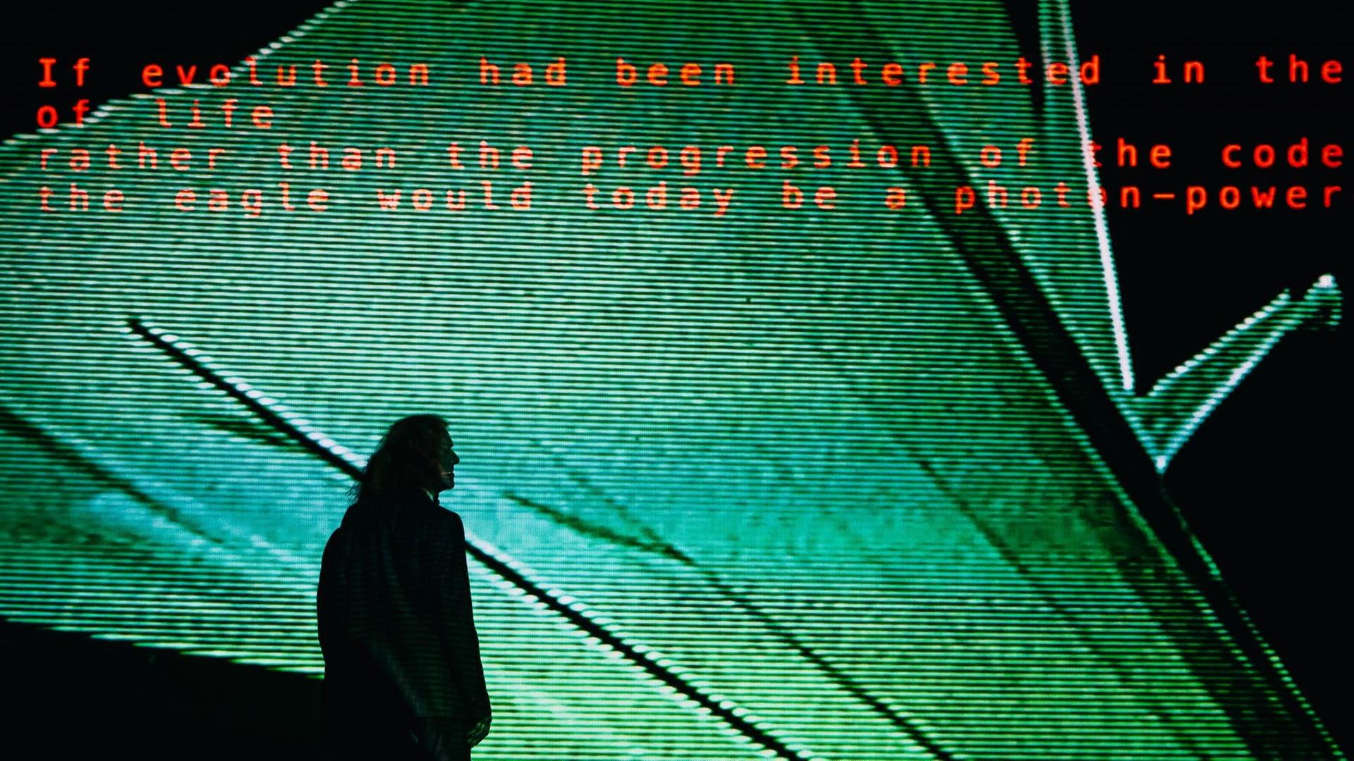 Ein Mann steht vor einem überdimensionalem Bildschirm, auf dem Text zu lesen ist. Ein Mann steht vor einem überdimensionalem Bildschirm, auf dem Text zu lesen ist.