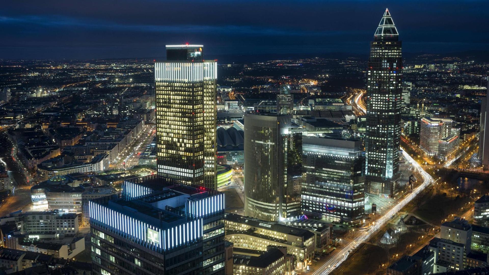 Skyline und Messe in Frankfurt am Main bei Nacht: Bürohäuser mit leuchtenden Fenstern sowie hell erleuchtete Straßen