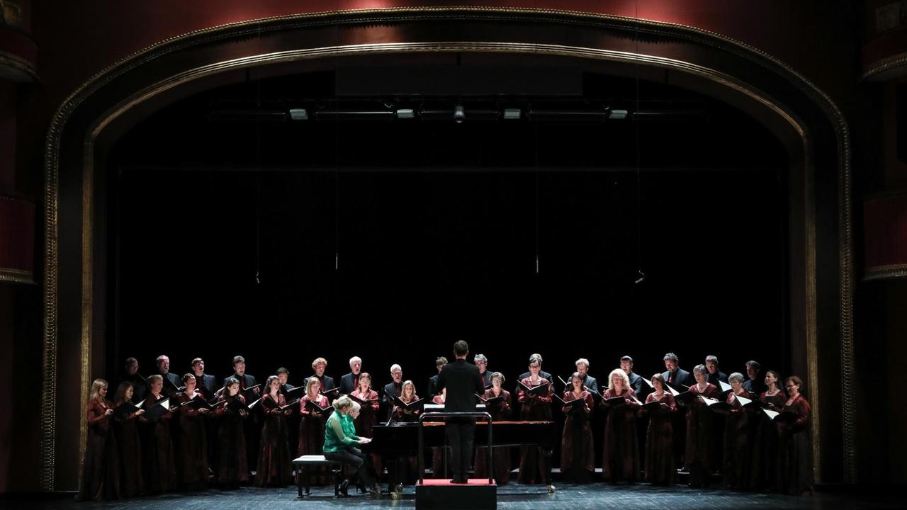 Der Chor steht auf einer großen Bühen, vor den Sängerinnen zwei Pianistinnen an einem Flügel Der Chor steht auf einer großen Bühen, vor den Sängerinnen zwei Pianistinnen an einem Flügel