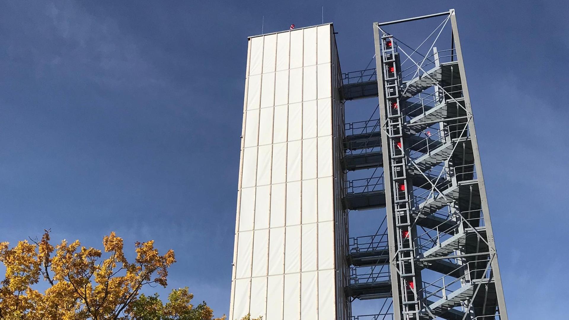 Auf dem Campus der Universität Stuttgart steht ein adaptives Hochhaus. Auf der linken Seite der eigentliche Turm mit einer Plastikfassade, rechts eine Stahltreppe
