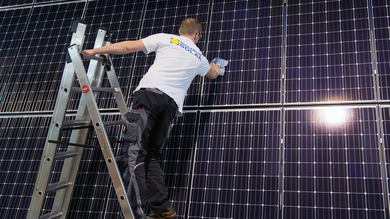 Ein Mitarbeiter einer Dresdner Solarfirma steht auf einer Leiter und legt letzte Hand an einer Photovoltaikanlage an, bei der die Solarzellen senkrecht an einer Wand angebracht sind.