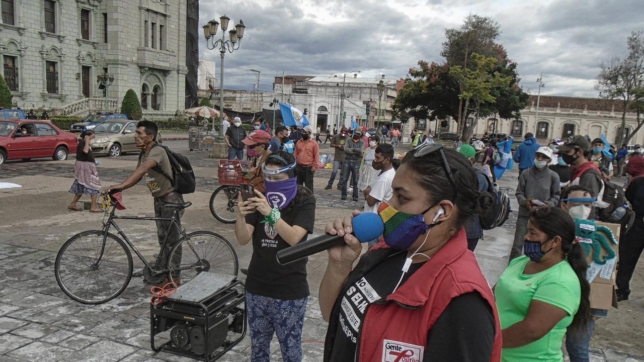 Demonstrierende in Guatemala-Stadt haben sich zum Protest gegen Korruption versammelt, eine Frau in roter Weste spricht in ein Mikrofon, alle tragen Mund-Nase-Masken und halten Abstand voneinander, um sich während der weltweiten Covid-19-Pandemie vor Ansteckung zu schützen. Demonstrierende in Guatemala-Stadt haben sich zum Protest gegen Korruption versammelt, eine Frau in roter Weste spricht in ein Mikrofon, alle tragen Mund-Nase-Masken und halten Abstand voneinander, um sich während der weltweiten Covid-19-Pandemie vor Ansteckung zu schützen.