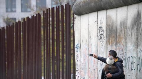 Ein Paar steht vor der Berliner Mauer und macht ein Selfie.