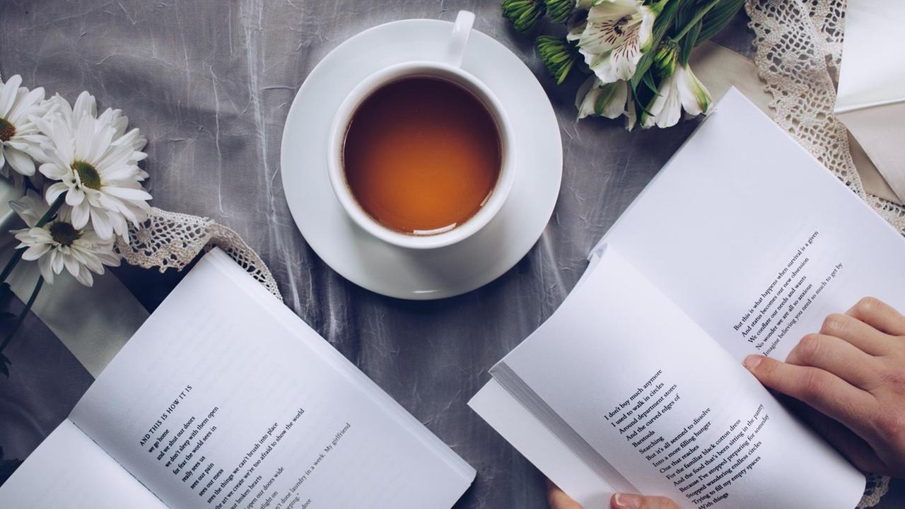 Ein aufgeschlagener Band mit einem Gedicht auf einem Tisch. Dazu eine Tasse Kaffee mit schöner Crema. Ein aufgeschlagener Band mit einem Gedicht auf einem Tisch. Dazu eine Tasse Kaffee mit schöner Crema.