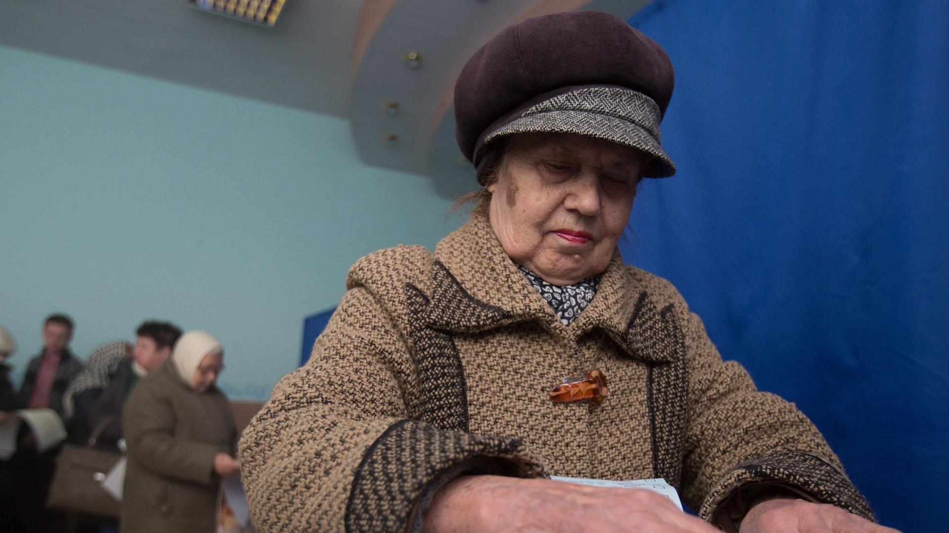 Eine ältere Frau steckt ihren Stimmzettel in eine Urne.