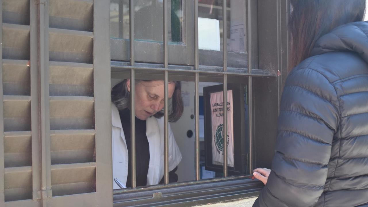 Frau steht vor einem Fenster mit Gitterstäben, dahinter die Apothekerin Frau steht vor einem Fenster mit Gitterstäben, dahinter die Apothekerin