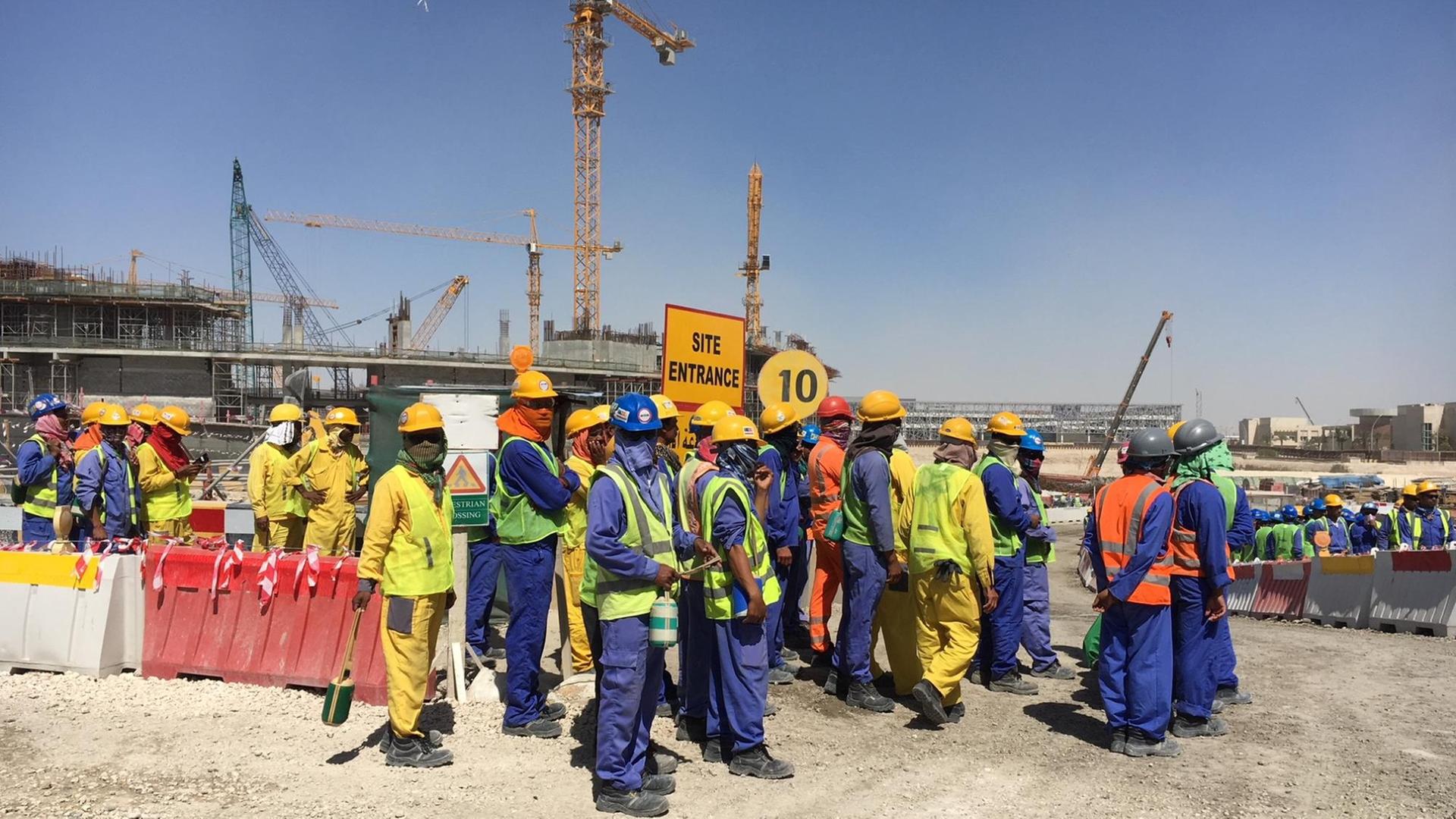 Bauarbeiter stehen auf riesiger Baustelle, das Gesicht mit Tüchern verpackt gegen die Hitze