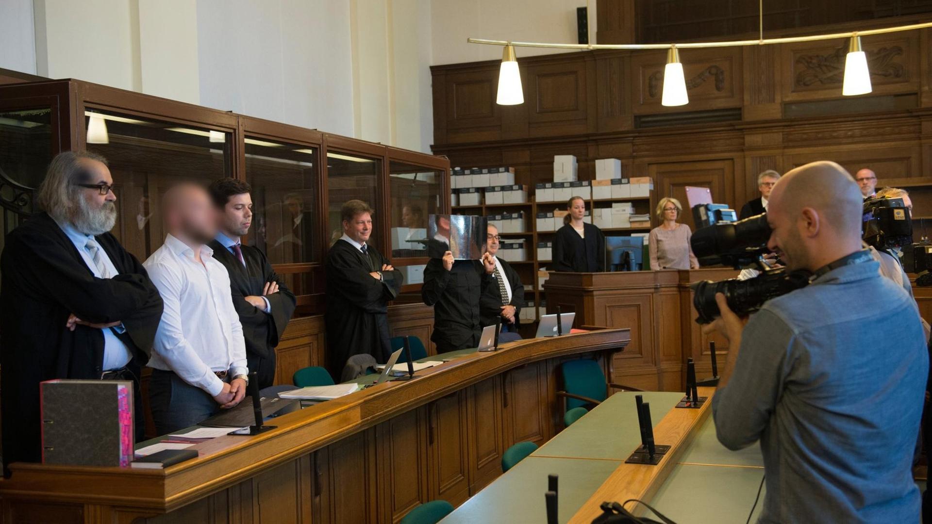 Sie sehen einen Gerichtssaal mit den beien Angeklagten und ihren Verteidigern. Die Gesichter der Angeklagten sind unscharf. Sie sehen einen Gerichtssaal mit den beien Angeklagten und ihren Verteidigern. Die Gesichter der Angeklagten sind unscharf.
