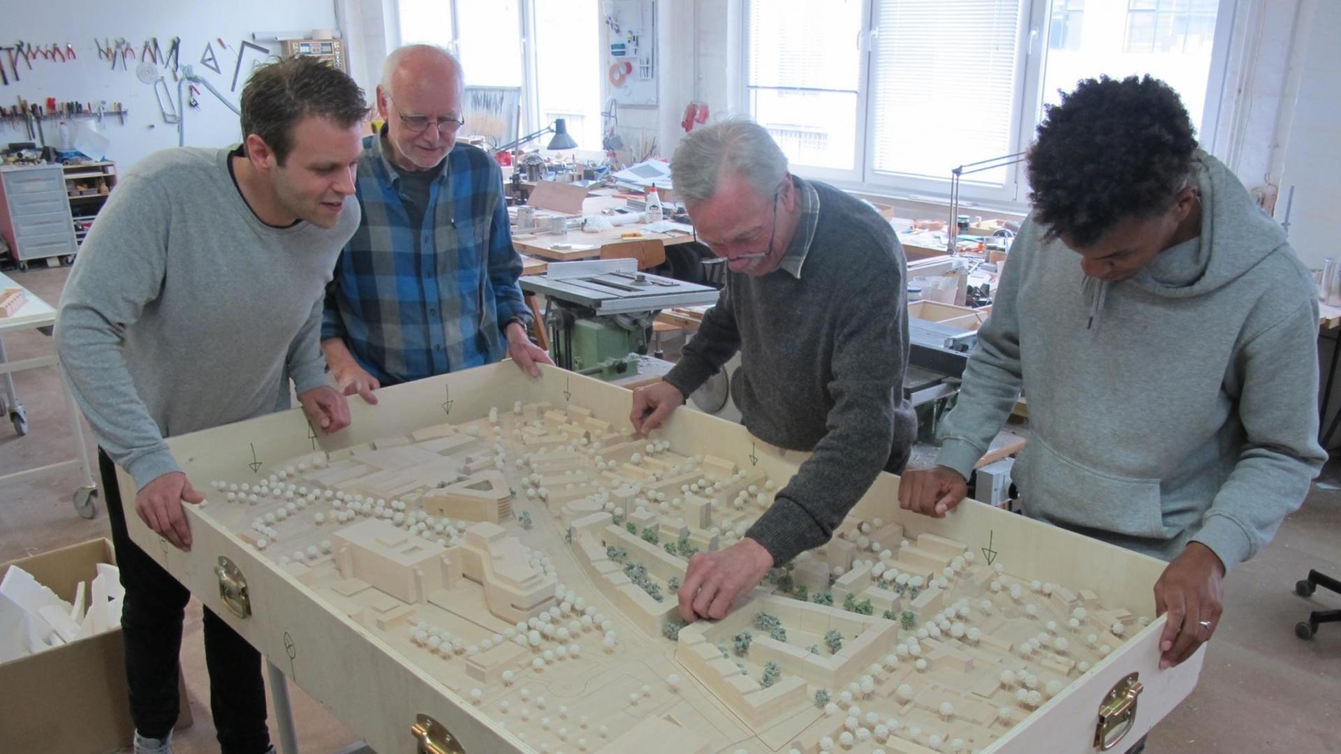 Das Team des Modellbauers WUB betrachtet das Modell einer Neubausiedlung, die aus Straßenzügen, Reihenhäusern, Mietshäusern und Gewerbegebäuden besteht.