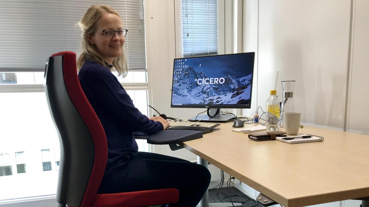 Eine junge blonde Frau mit Brille sitzt an ihrem Schreibtisch, auf dem nur einige Getränke stehen. Ihre Hände liegen auf der Tastatur ihres Computers, auf dessen Bildschirm mit großen Buchstaben "Cicero" steht. Eine junge blonde Frau mit Brille sitzt an ihrem Schreibtisch, auf dem nur einige Getränke stehen. Ihre Hände liegen auf der Tastatur ihres Computers, auf dessen Bildschirm mit großen Buchstaben "Cicero" steht.