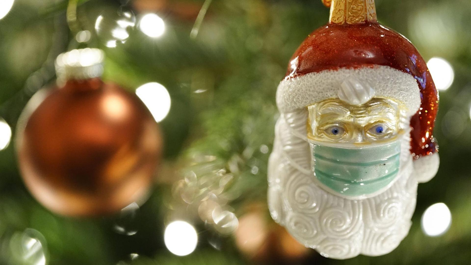 An einem Weihnachtsbaum hängt eine Weihnachtsmann-Figur mit Mundschutz.