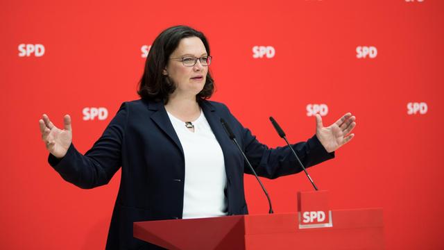 Andrea Nahles, Vorsitzende der Sozialdemokratischen Partei Deutschlands, SPD, steht mit offenen Armen an einem Rednerpult vor einem roten Hintergrund mit SPD-Logo.