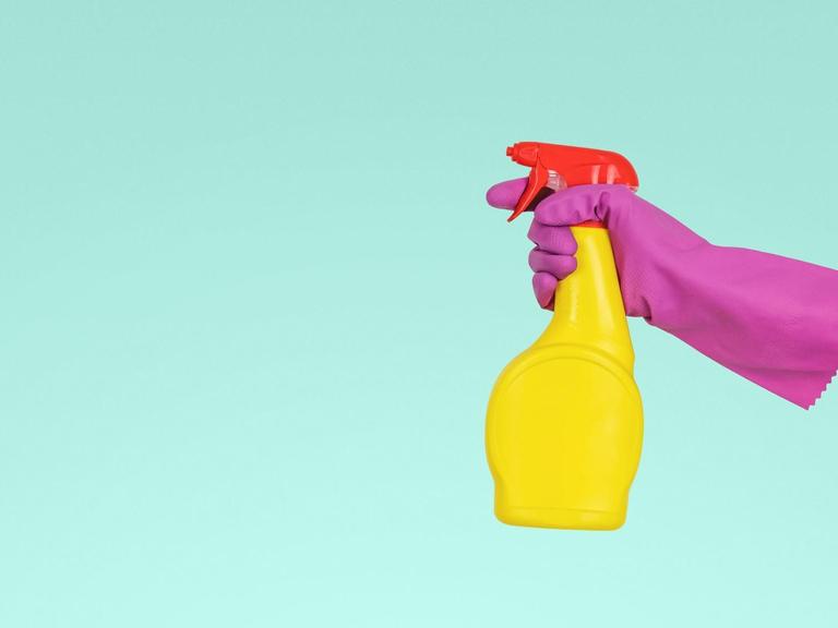 Eine gummibehandschuhte Hand hält eine Sprühflasche mit Putzmittel.