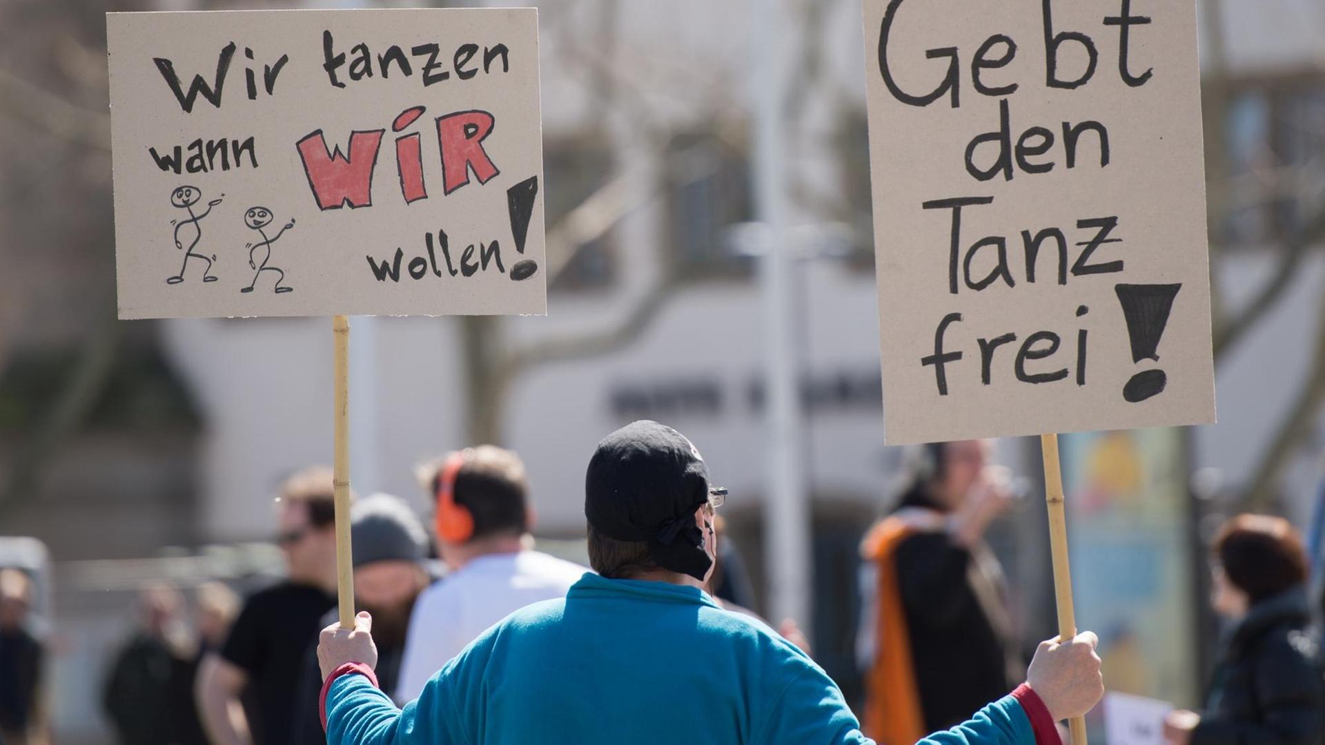 Ein Teilnehmer einer von der Piratenpartei organisierten Versammlung gegen das Tanzverbot hält am 03.04.2015 in Stuttgart (Baden-Württemberg) Schilder mit der Aufschrift "Wir tanzen wann wir wollen!" und "Gebt den Tanz frei". Aus Protest gegen das Tanzverbot hörten die Versammelten Musik über Kopfhörer, einige tanzten dazu.