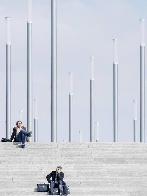 Männer in Anzügen sitzen auf betongrauen Treppenstufen.