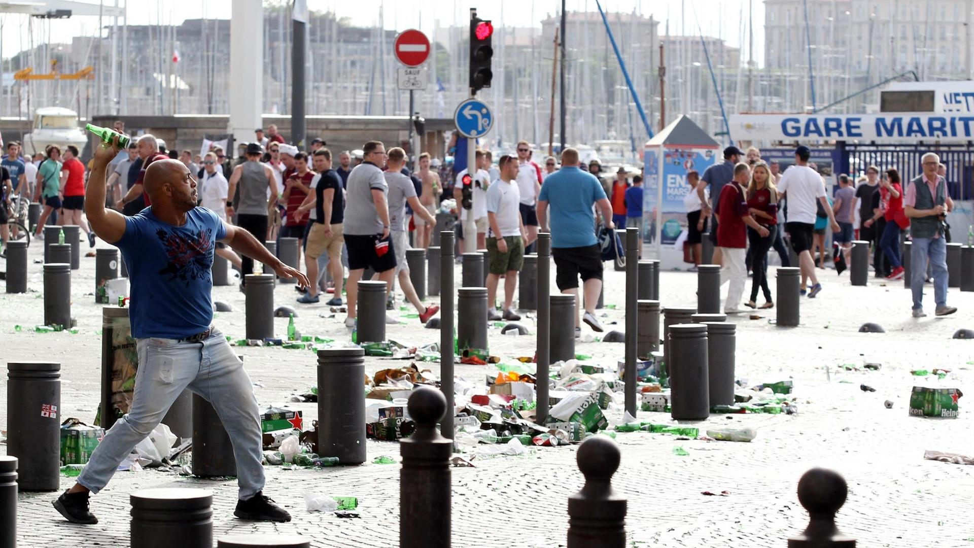 Ein Mann wirft eine Flasche, auf den Straßen liegt Müll, im Hintergrund Menschen.