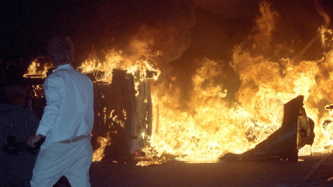 Ein Mann steht am 27.08.1992 vor brennenden Pkw auf einer Straße am zentralen Asylbewerberheim von Mecklenburg-Vorpommern in Rostock-Lichtenhagen. Vom 22. bis 28. August 1992 randalierten bis zu 1.200 meist jugendliche rechtsradikale Gewalttäter vor dem Zentralen Asylbewerberheim Mecklenburg-Vorpommern in Rostock-Lichtenhagen. Unter dem Beifall von bis zu 3000 Schaulustigen und vielen Fernsehkameras bewarfen die Rowdies das überwiegend mit Rumänen belegte Hochhaus (Sonnenblumenhaus) sowie die Polizisten mit Steinen und Brandsätzen. Foto: Bernd Wüstneck | Verwendung weltweit Ein Mann steht am 27.08.1992 vor brennenden Pkw auf einer Straße am zentralen Asylbewerberheim von Mecklenburg-Vorpommern in Rostock-Lichtenhagen. Vom 22. bis 28. August 1992 randalierten bis zu 1.200 meist jugendliche rechtsradikale Gewalttäter vor dem Zentralen Asylbewerberheim Mecklenburg-Vorpommern in Rostock-Lichtenhagen. Unter dem Beifall von bis zu 3000 Schaulustigen und vielen Fernsehkameras bewarfen die Rowdies das überwiegend mit Rumänen belegte Hochhaus (Sonnenblumenhaus) sowie die Polizisten mit Steinen und Brandsätzen. Foto: Bernd Wüstneck | Verwendung weltweit