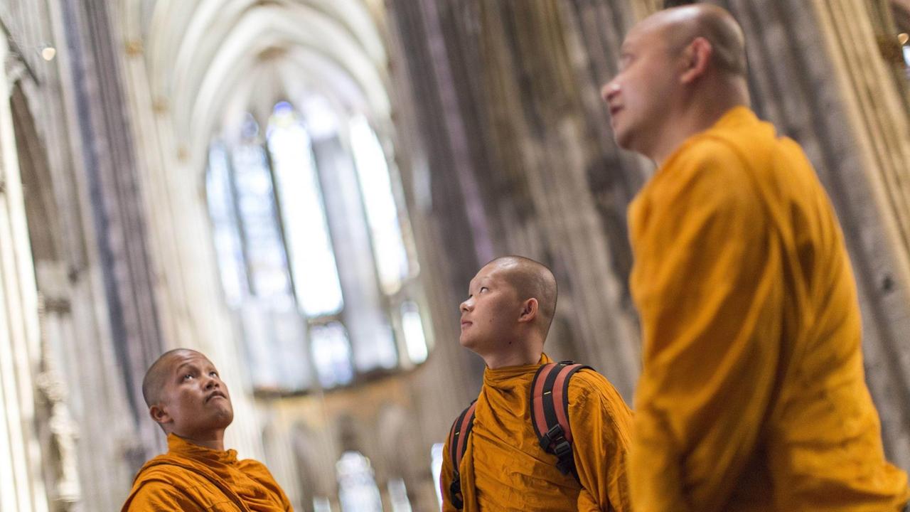 Drei buddhistische Mönche in orangenen Roben besuchen den Kölner Dom.