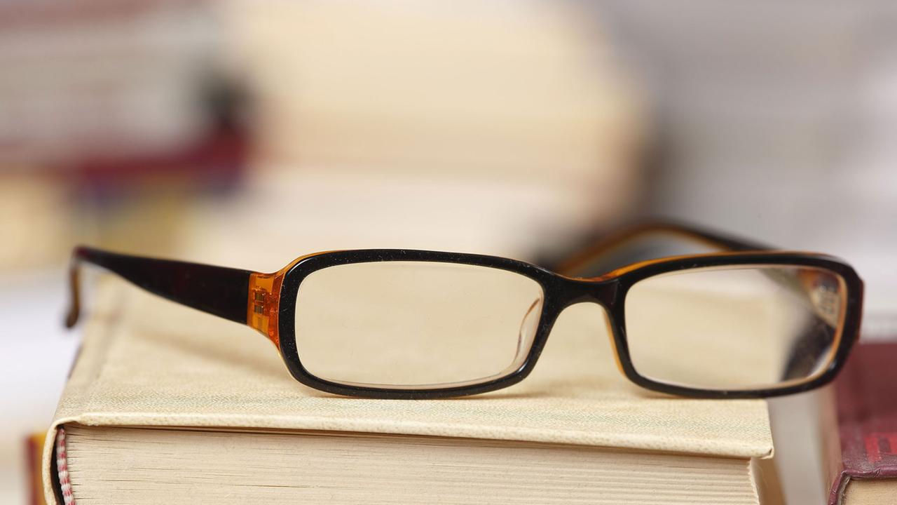 Eine Lesebrille liegt auf einem Bücherstapel. Eine Lesebrille liegt auf einem Bücherstapel.