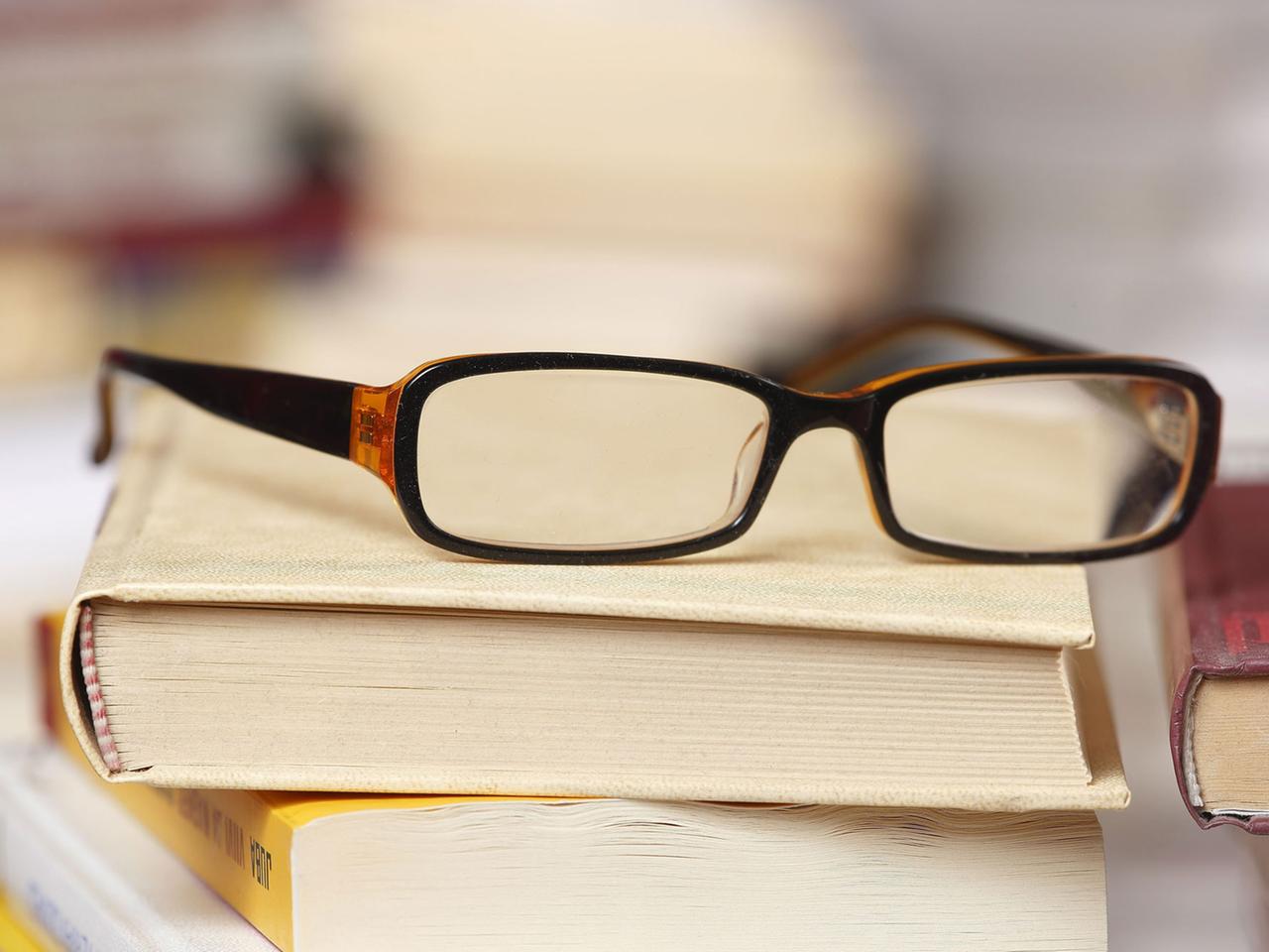 Eine Lesebrille liegt auf einem Bücherstapel. Eine Lesebrille liegt auf einem Bücherstapel.