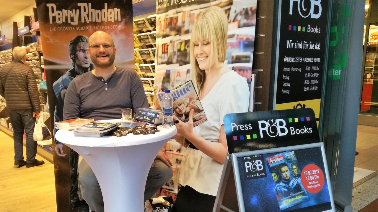 Kai Hirdt an einem Stehtisch in einer Buchhandlung, Schild: Signierstunde Kai Hirdt an einem Stehtisch in einer Buchhandlung, Schild: Signierstunde