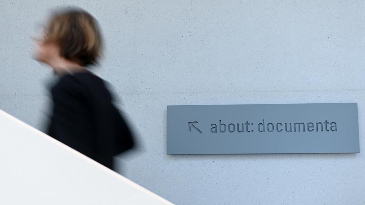 19.11.2019, Hessen, Kassel: Eine Frau geht zur Vorbesichtigung der Dauerausstellung "about: documenta" in der Neuen Galerie an einem Hinweisschild mit der Aufschrift "about: documenta" vorbei. Die Schau soll anhand originaler documenta-Kunstwerke und verschiedener Dokumente die Geschichte der bedeutendsten Ausstellung für zeitgenössische Kunst beleuchten. 19.11.2019, Hessen, Kassel: Eine Frau geht zur Vorbesichtigung der Dauerausstellung "about: documenta" in der Neuen Galerie an einem Hinweisschild mit der Aufschrift "about: documenta" vorbei. Die Schau soll anhand originaler documenta-Kunstwerke und verschiedener Dokumente die Geschichte der bedeutendsten Ausstellung für zeitgenössische Kunst beleuchten.