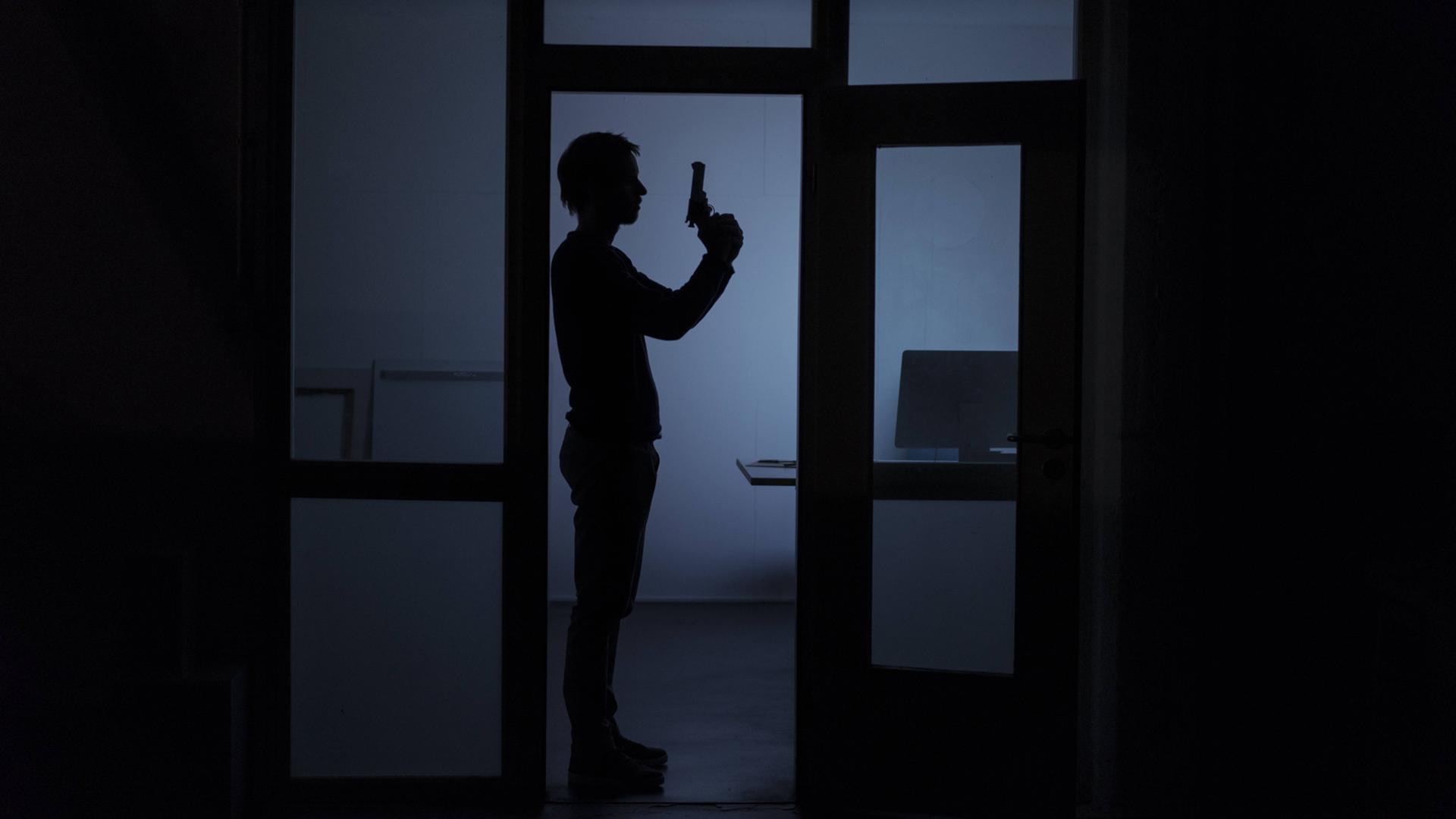 Ein Mann mit Pistole steht nachts in einem Büro.