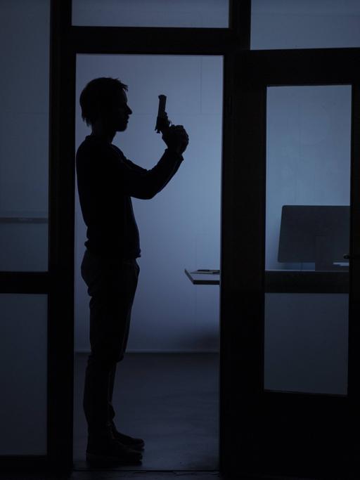 Ein Mann mit Pistole steht nachts in einem Büro.