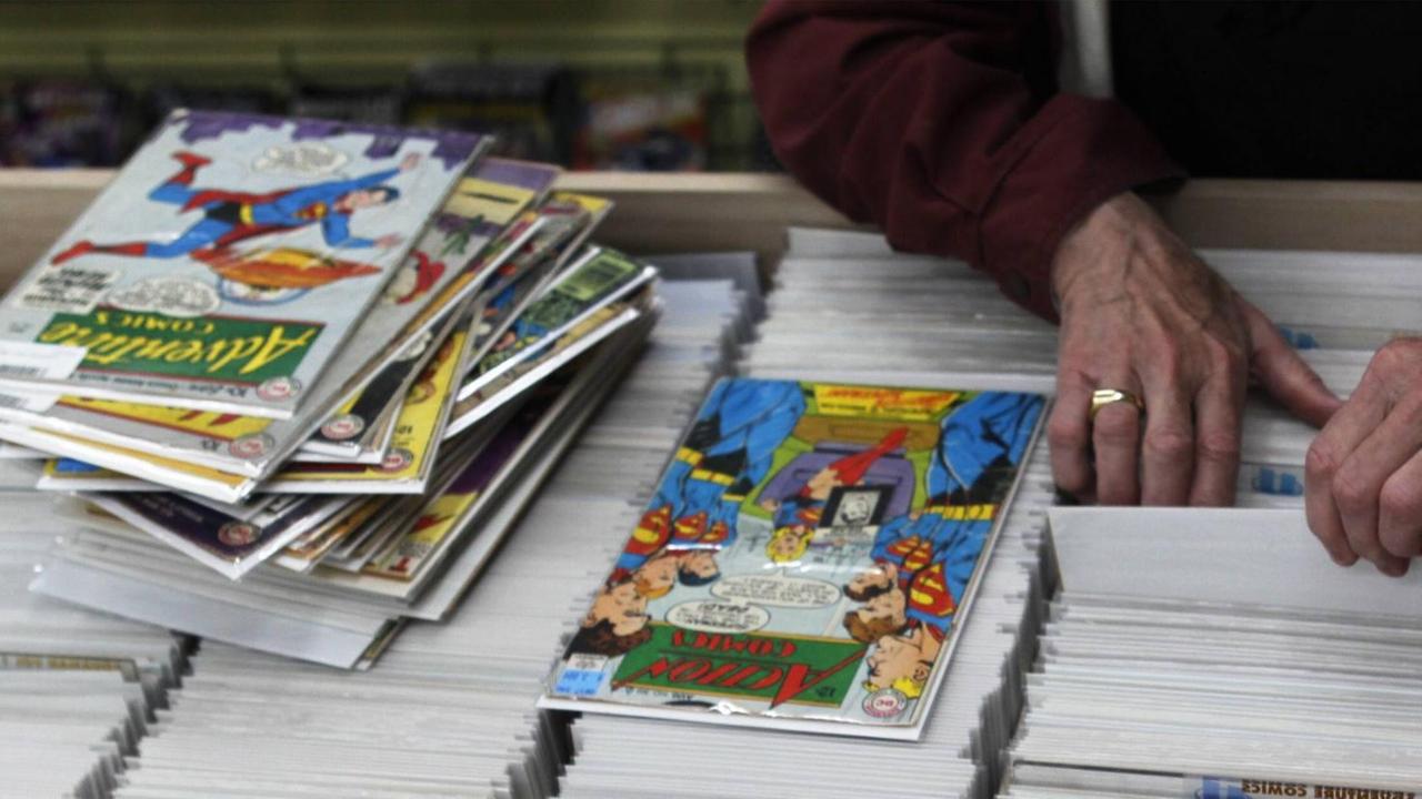 Ein Mann durchsucht eine Auslage mit Comic-Heften in einem Comic-Shop in der US-Stadt Cincinnati. Auf der Auslage befindet sich bereits ein Stapel Comics. Ein Mann durchsucht eine Auslage mit Comic-Heften in einem Comic-Shop in der US-Stadt Cincinnati. Auf der Auslage befindet sich bereits ein Stapel Comics.