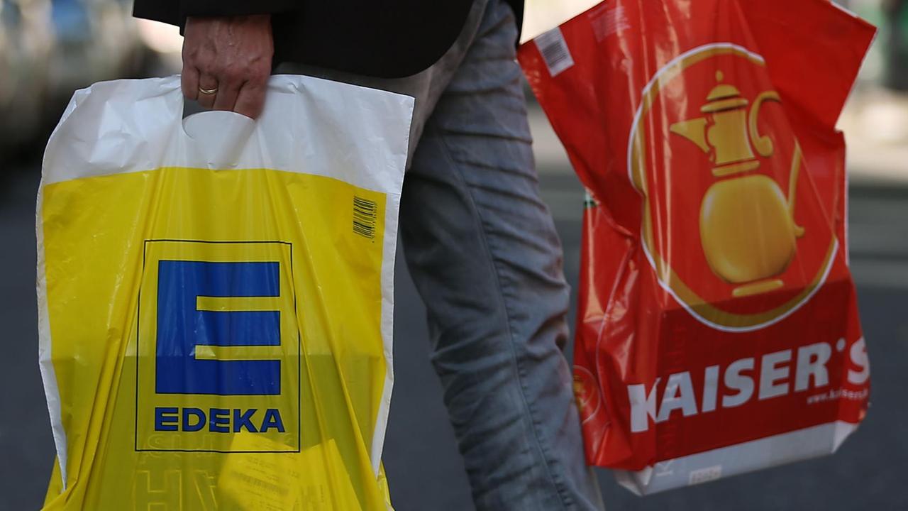 Ein Mann geht mit jeweils einer Tüte von Edeka und Kaiser's über die Straße. Ein Mann geht mit jeweils einer Tüte von Edeka und Kaiser's über die Straße.