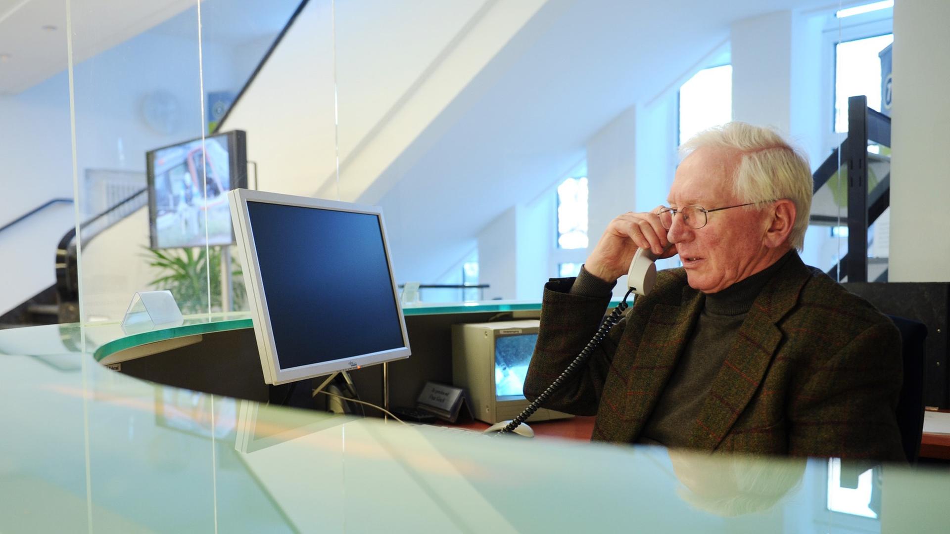 Ein Senior sitzt im Büro an einem Empfang und telefoniert. Ein Senior sitzt im Büro an einem Empfang und telefoniert.