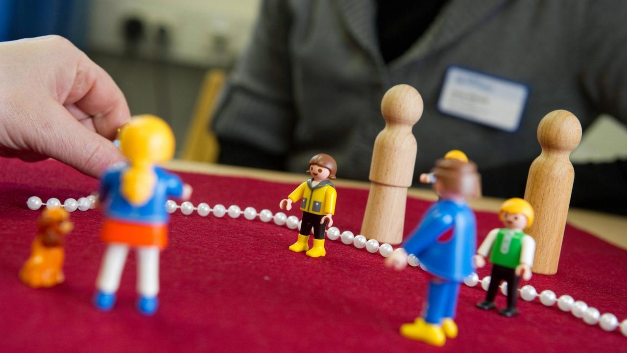 Zu sehen sind mehrere Playmobil-Figuren sowie einfache Holz-Figuren, die von einer Person auf einem Tisch aufgestellt werden.