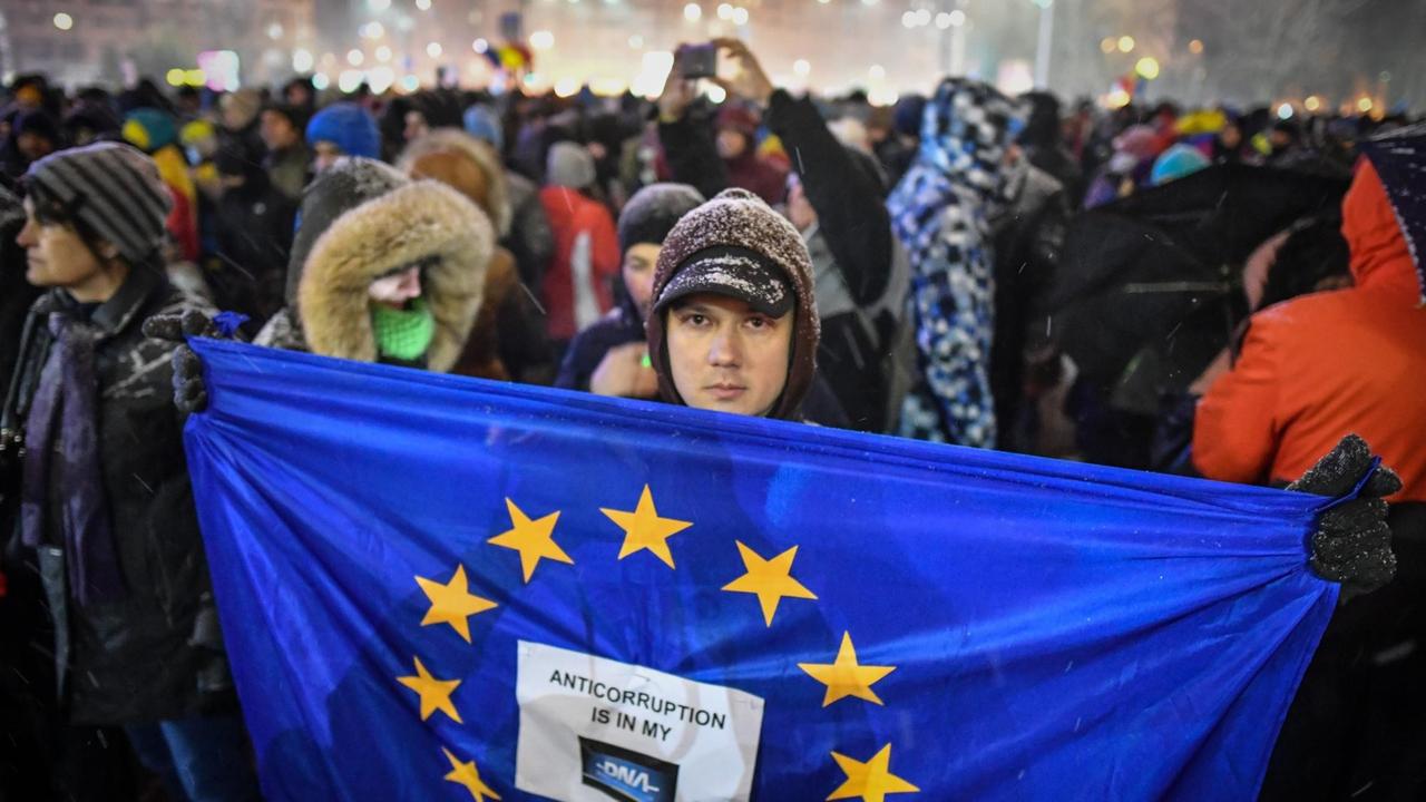 In Bukarest demonstrieren tausende Menschen gegen Korruption. Ein Mann hält eine EU-Flagge in die Kamera. In Bukarest demonstrieren tausende Menschen gegen Korruption. Ein Mann hält eine EU-Flagge in die Kamera.