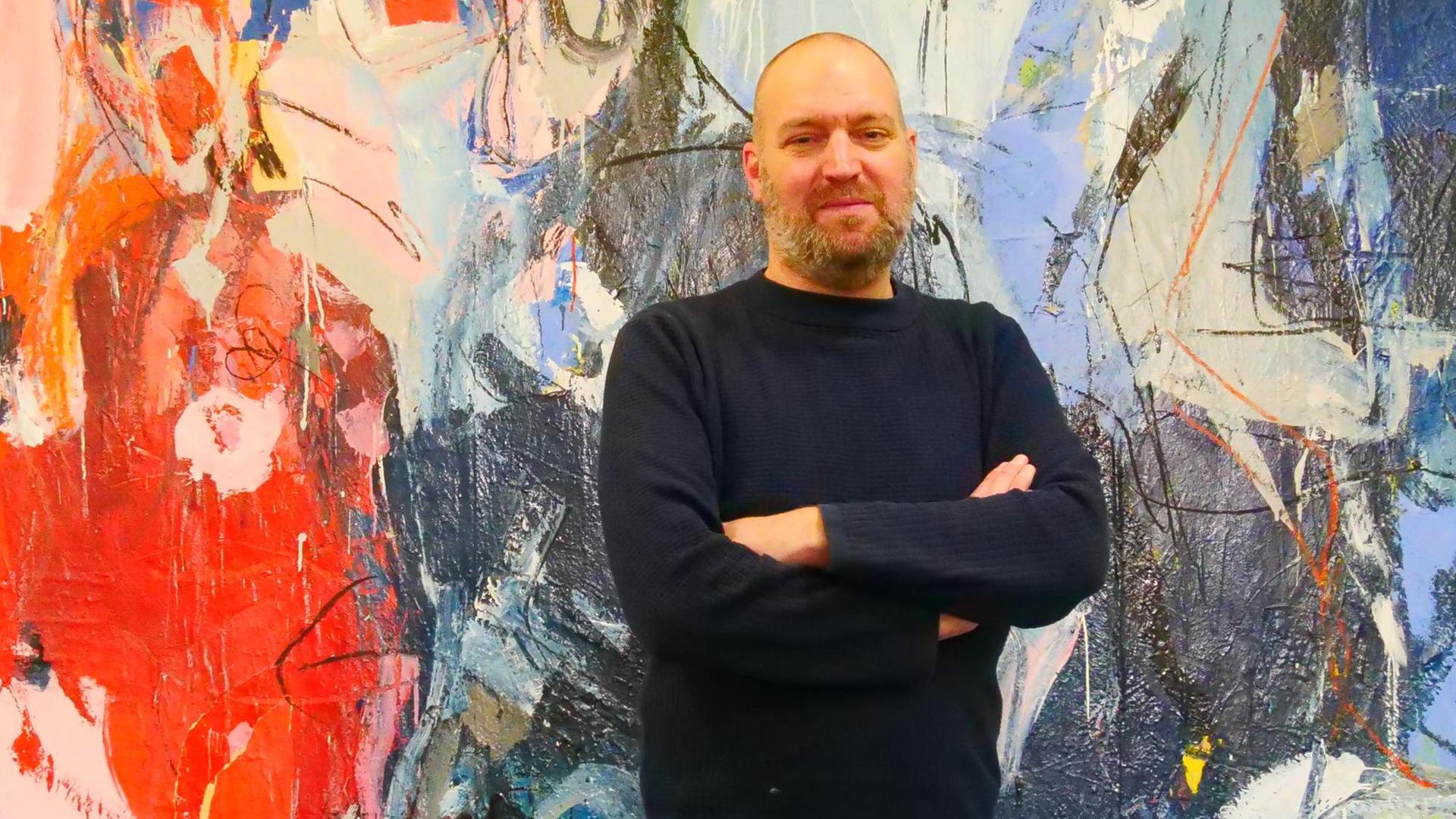 Felix Scharlau - Autor des Romans "Du bist es vielleicht" - vor einem bunten Gemälde im DLF-Funkhaus