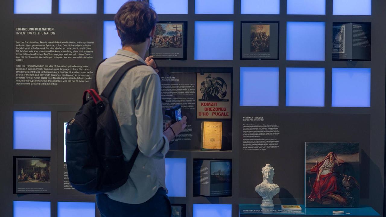 Einblick in die Ausstellung des Dokumentationszentrums Flucht, Vertreibung, Versöhnung im Deutschlandhaus in Berlin. Ein Mann steht vor einer Wand mit kleinen quadratischen drehbaren Schautafel-Würfeln und Schaukästen mit Objekten zum Bereich "Erfindung der Nation" in der Ausstellung. Einblick in die Ausstellung des Dokumentationszentrums Flucht, Vertreibung, Versöhnung im Deutschlandhaus in Berlin. Ein Mann steht vor einer Wand mit kleinen quadratischen drehbaren Schautafel-Würfeln und Schaukästen mit Objekten zum Bereich "Erfindung der Nation" in der Ausstellung.