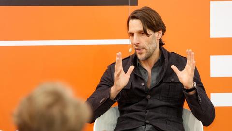 Philipp Hübl sitzt auf der Bühne von Deutschlandfunk Kultur mit Mikrofon und gestikuliert.