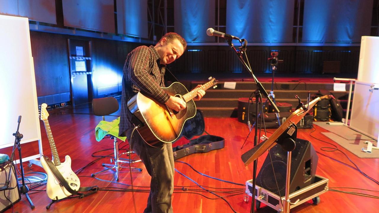 Ein Mann mit dunklen Haaren spielt mit geschlossenen Augen Akustik-Gitarre Ein Mann mit dunklen Haaren spielt mit geschlossenen Augen Akustik-Gitarre